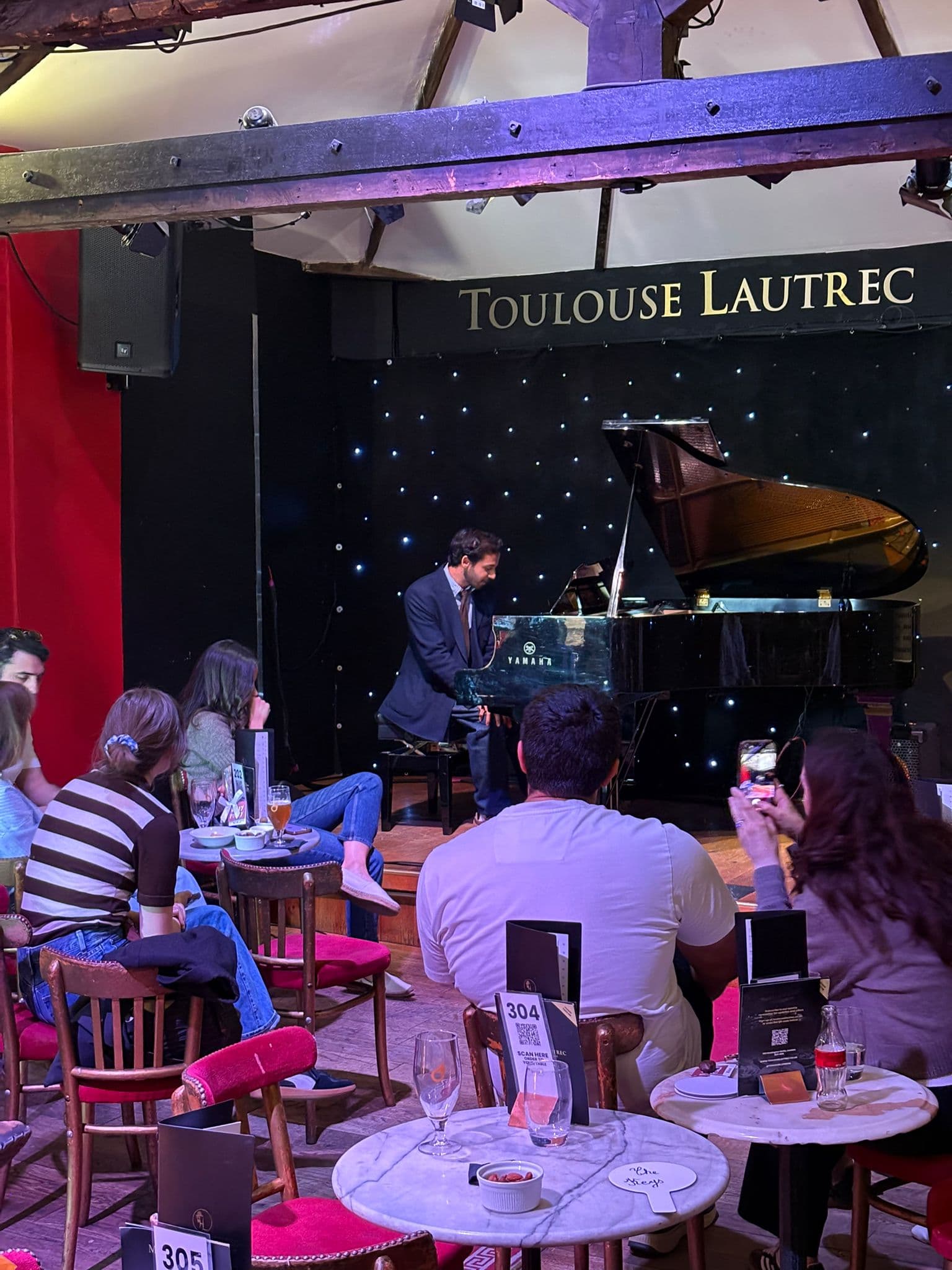 A student playing the grand piano for the audience at the Toulouse Lautrec Jazz Club